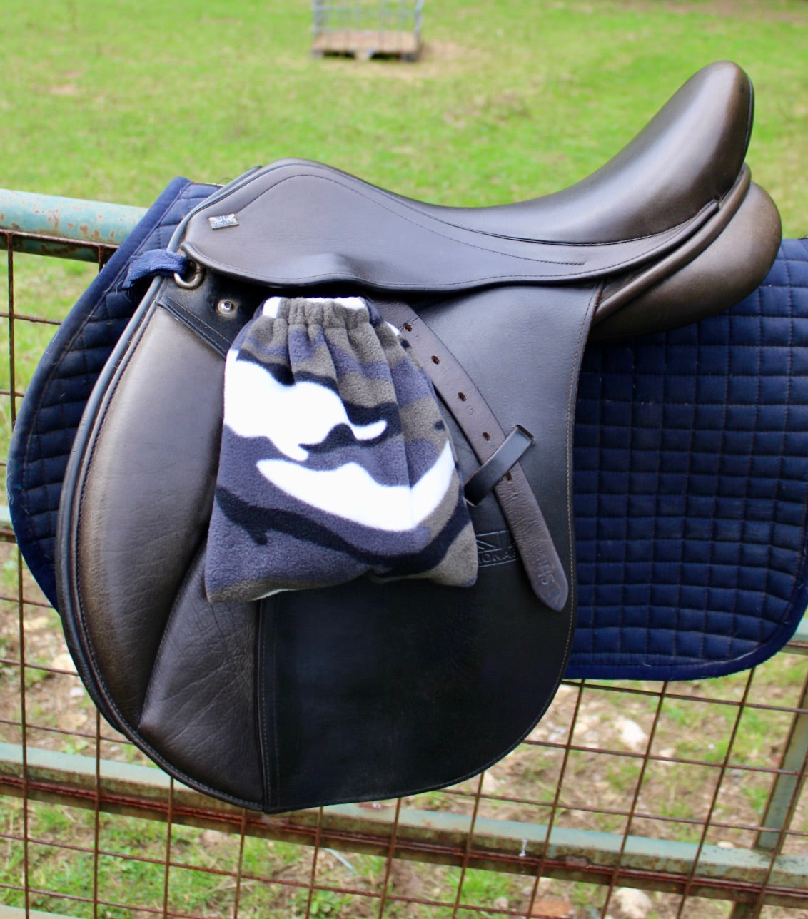 camouflage patterned stirrup covers, on a brown monarch saddle which has a navy le Mieux saddle pad under, on a field fence