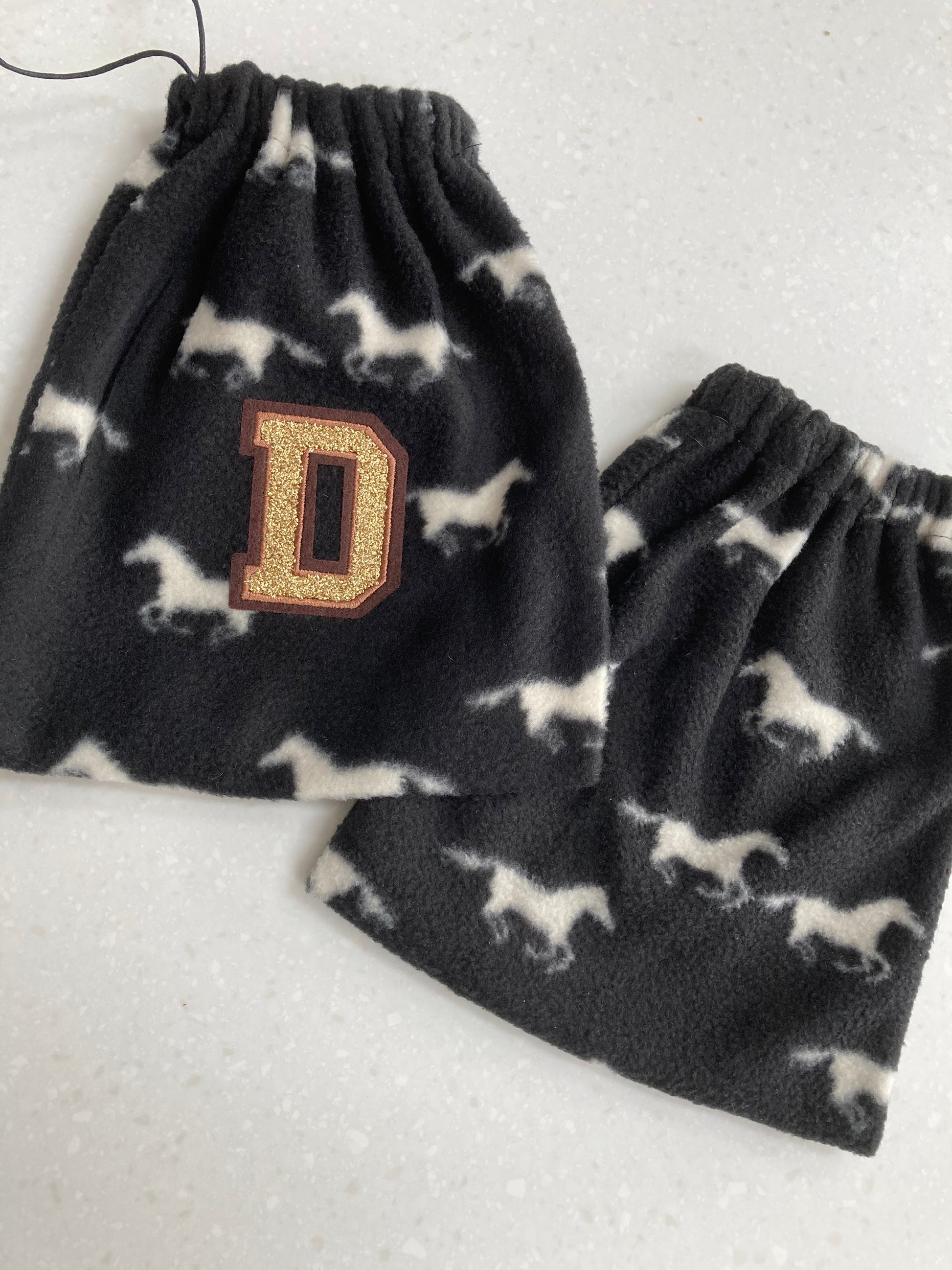 black stirrup covers with white horses on them and a gold 'd' embroidered patch on one of them